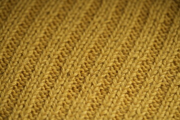 macro texture of yellow knitted wool fabric. The soft and cozy hand-knitted textile features a ribbed pattern with visible yarn loops and detailed stitches. Ideal background for fashion, textile