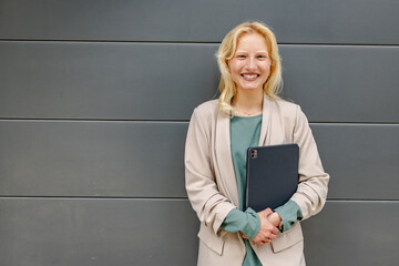 Albino woman smiling confidently while holding a tablet against a modern gray backdrop during...