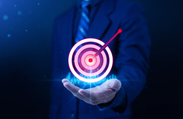 Businessman hand holding glowing target with arrow pointing towards the target which symbolizes...
