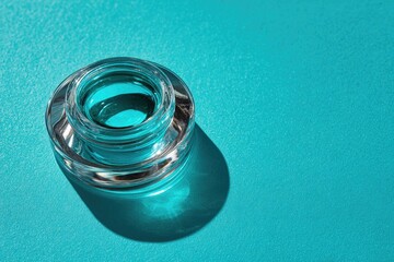 Clear glass cosmetic jar on teal background