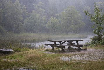 table de pique nique au bord d'un lac en pleine nature sous une averse. Violent orage avec...