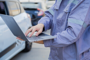 Mechanic in uniform using laptop outdoors beside car, modern automotive technology, digital diagnostic tools, and professional maintenance process showing integration of online systems, car insurance