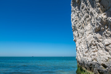 A white chalk cliff rising from the edge of a calm blue sea under a clear sky at Kingsgate Bay in Broadstairs, England