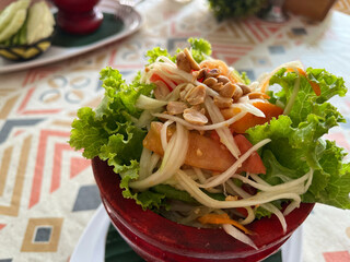 Somtum Thai papaya salad in red bowl on table