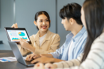 Confident asian businesswoman leading a marketing presentation during a team meeting, holding a chart while discussing ideas and visual data in a collaborative marketing presentation