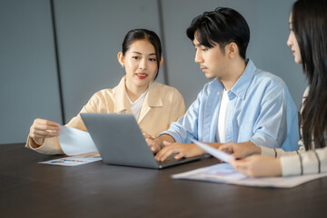 Three coworkers review printed reports and digital charts during a meeting, focusing on data analysis for project strategy, making data analysis central to collaborative decision making.