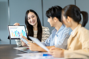Young asian woman presenting a financial report during a team meeting in a modern office, discussing data charts and analysis to support the financial report and marketing goals