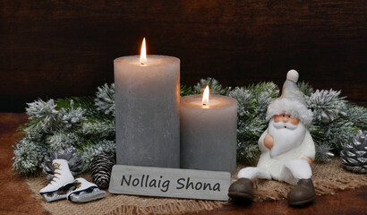 Christmas greeting card: Arrangement with candles, Christmas balls and a Santa Claus, a sign is inscribed with the Irish text Nollaig Shona.