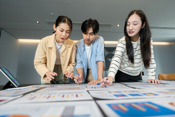 Group of asian professionals discussing charts during a business meeting, working together around a table to achieve results through effective business collaboration.	
