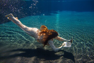 Businesswoman working with laptop underwater in swimming pool