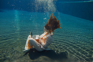 Businesswoman working underwater with laptop in swimming pool