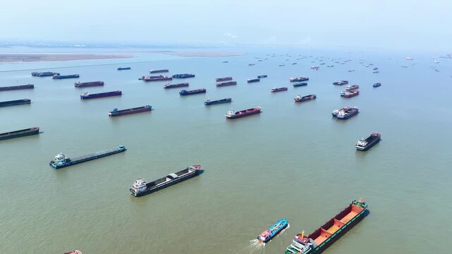Multiple dry cargo vessels ships anchored waiting for port entrance to loading in industrial port, reflecting slowdown freight traffic, backlog of ships waiting to unload due to imposed trade barriers