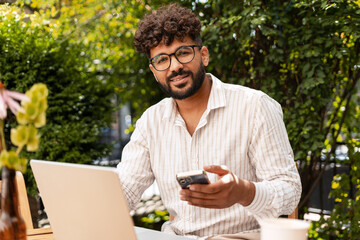 Entrepreneur working remotely using laptop and smartphone in a bar garden