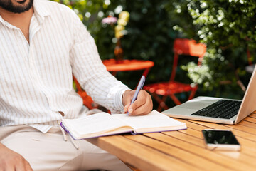 Businessman writing notes in notebook while working remotely in cafe
