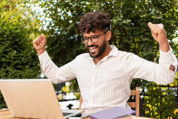 Excited businessman celebrating success while working on laptop outdoors