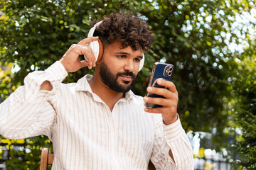 Young man listening music with headphones and holding smartphone in park