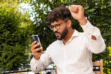 Excited businessman celebrating success while looking at smartphone outdoors