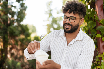 Smiling man opening yogurt cup in a garden