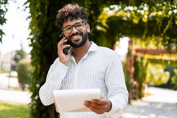 Smiling businessman talking on smartphone and holding document in park
