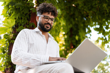 Indian freelancer working on laptop in a park during summer day