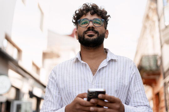 Pensive young manager using smartphone walking in the city center