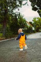 Fototapeta premium A cheerful child in colorful rain gear joyfully runs down a peaceful country road, exploring the lush greenery and surroundings, filled with excitement and curiosity about the world ahead