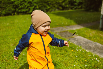An energetic child, dressed in colorful rain gear, is joyfully playing outside on a bright and...