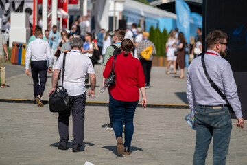 Crowd of people walking outdoors during a business event on a clear sunny day.