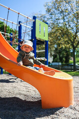 A joyful toddler slides down a bright orange playground slide on a sunny day, radiating excitement...