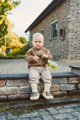 An adorable toddler is sitting peacefully on the steps while holding a beautiful leaf in hand,...