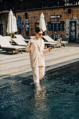 Businesswoman walking in pool with laptop and cocktail