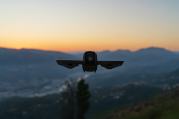 An FPV camera drone soars through the air, capturing stunning aerial views of a mountain range at a picturesque golden sunset.