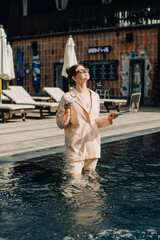 Businesswoman working remotely from swimming pool with laptop and cocktail