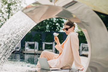 Businesswoman working remotely by the pool with cocktail and laptop