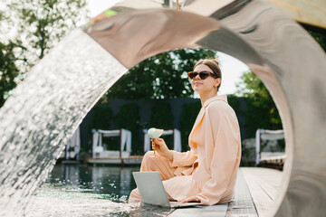 Businesswoman working poolside with laptop and cocktail enjoying summer vacation
