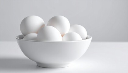 White ceramic bowl containing six white eggs, placed on a flat white surface against a plain white background
