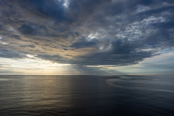 Dramatic cloudy sky over calm sea at sunset, scenic seascape with moody atmosphere and natural light reflections.

