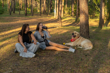 Two girls are walking with retriever dog in the pine forest.