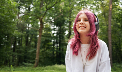 Young relaxed girl listening music with headphones in forest
