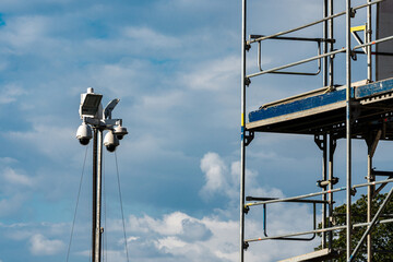 Security cameras are positioned on a pole to oversee a construction site with scaffolding. The...