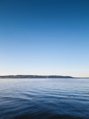 Lake in the morning. Camera close to calm water surface of the big lake shortly after sunrise. Gradient sky above montane bank of the river.