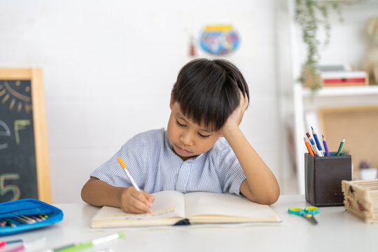 Asian boy studying with pencil at home smiling writing with notebook and school supplies, online learning, creative study in homeschooling, tutoring and learning course, kids education development - Powered by Adobe