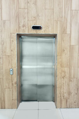 Closed metal elevator doors against a wooden wall.