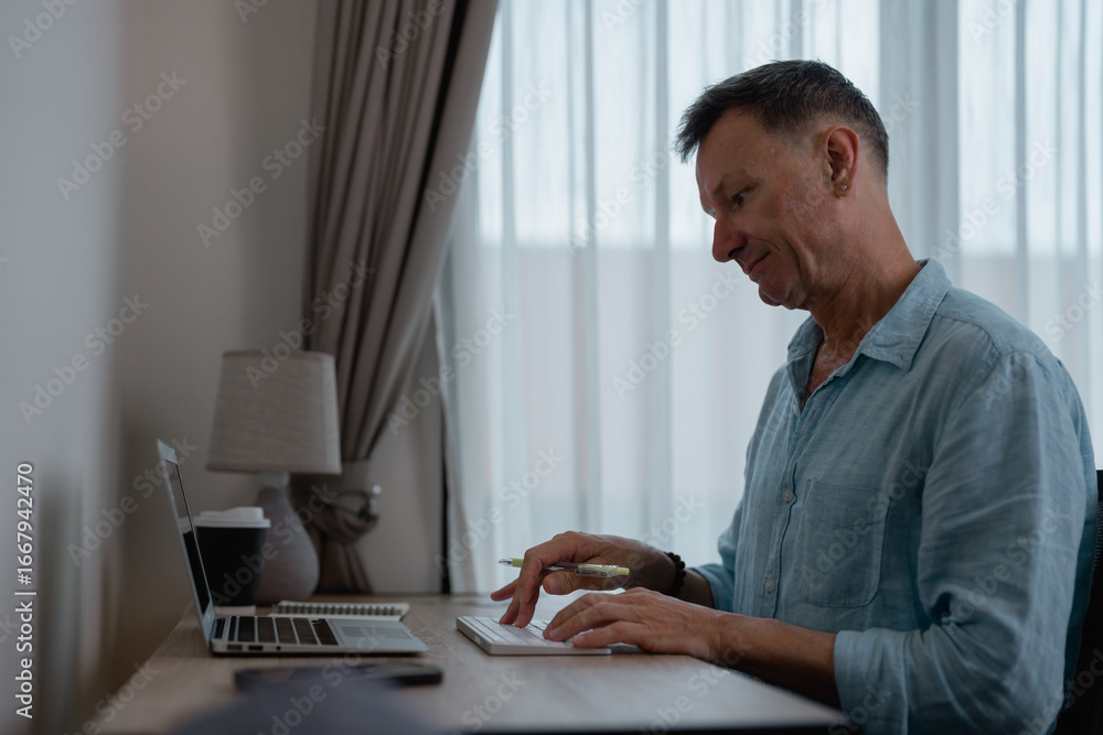 Poster senior caucasian man using computer keyboard and holding pen while working from home office sitting 