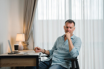 Pensive mature businessman working from home sitting at desk with laptop and holding pen, thinking...