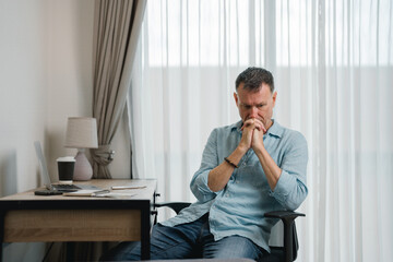 Stressed businessman sitting at his desk with hands clasped, experiencing anxiety and stress while...