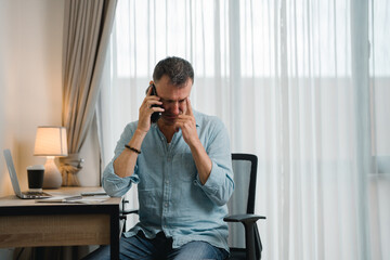 Worried businessman rubbing his forehead while receiving bad news on the phone during working from...
