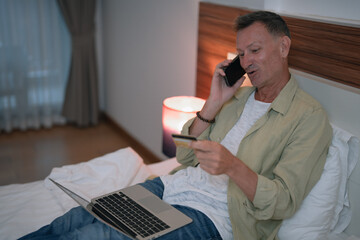 Mature businessman is making an online payment using his laptop and credit card while talking on...