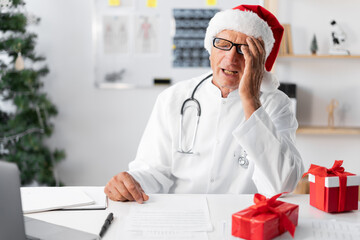 Senior elderly Doctor in Santa hat on the shift on christmas eve with epic fail mistaken omg gesture