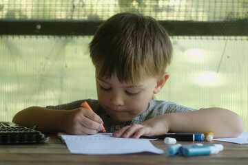 Small child draws with felt tip pens on piece of paper in summer gazebo